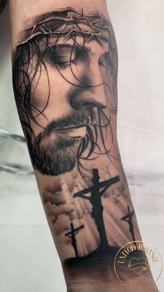 Tatuagem realista de Jesus com coroa de espinhos no braço.