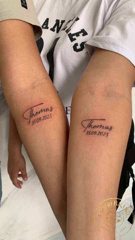 Tatuagem de pai e mãe homenageando filho com nome e data de nascimento.